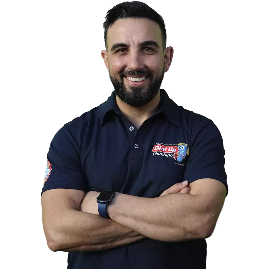 Smiling man with a beard in a navy Dial Up Plumbing polo shirt, standing with arms crossed.